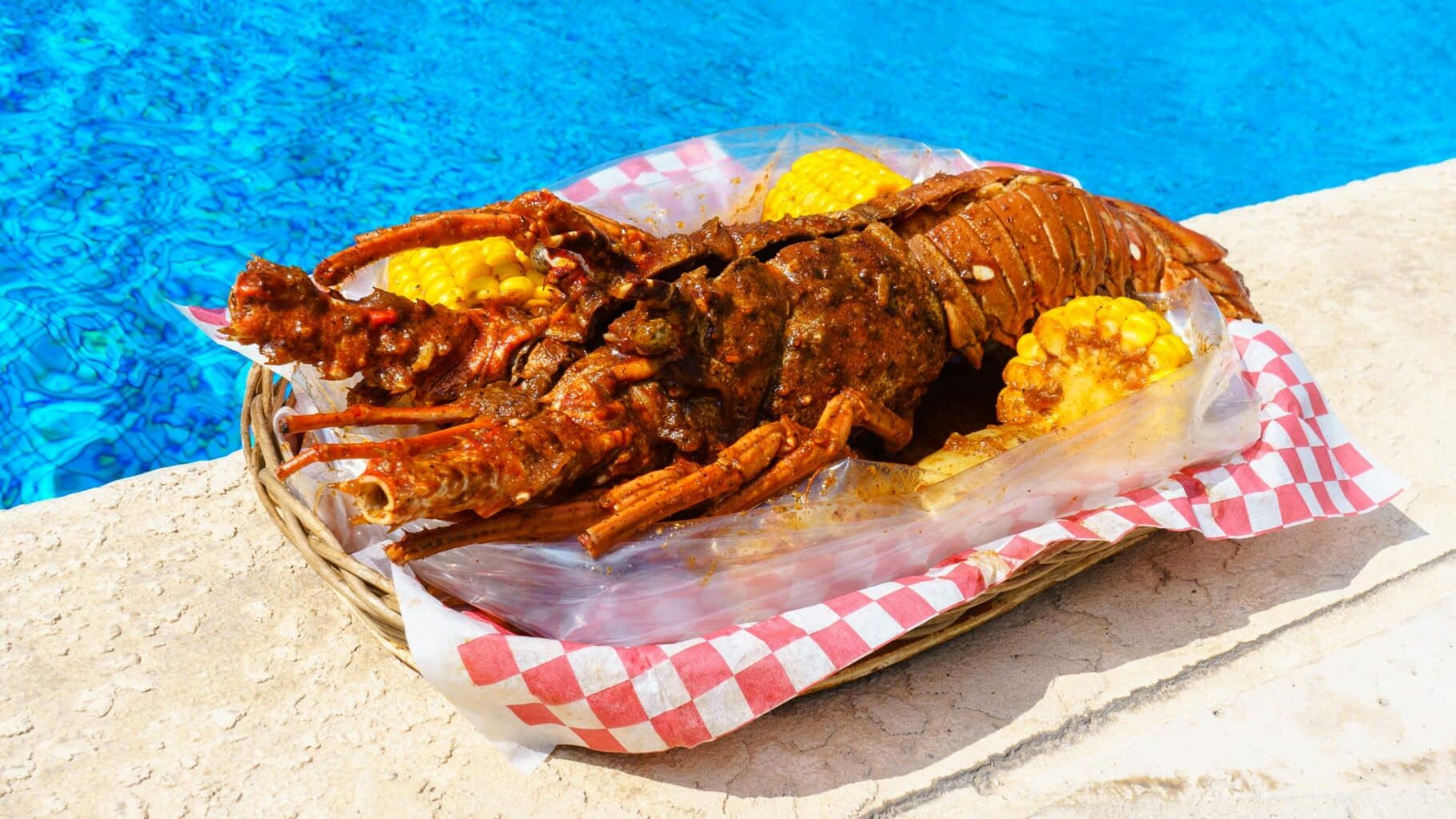 Sizzling grilled lobster with corn on the cob by a vibrant blue poolside, perfect summer delicacy.