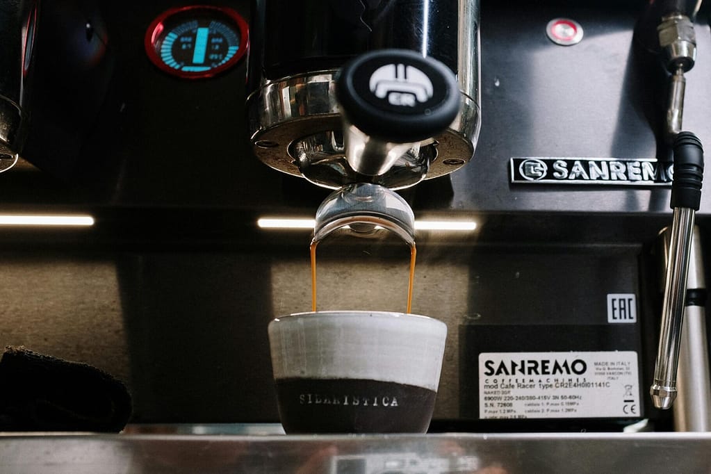 Close-up of espresso being poured into a ceramic cup from a Sanremo machine at a café.