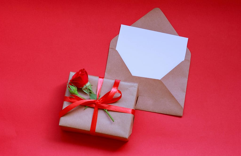 Brown gift box with a red rose and envelope on a vibrant red background, perfect for romantic celebrations