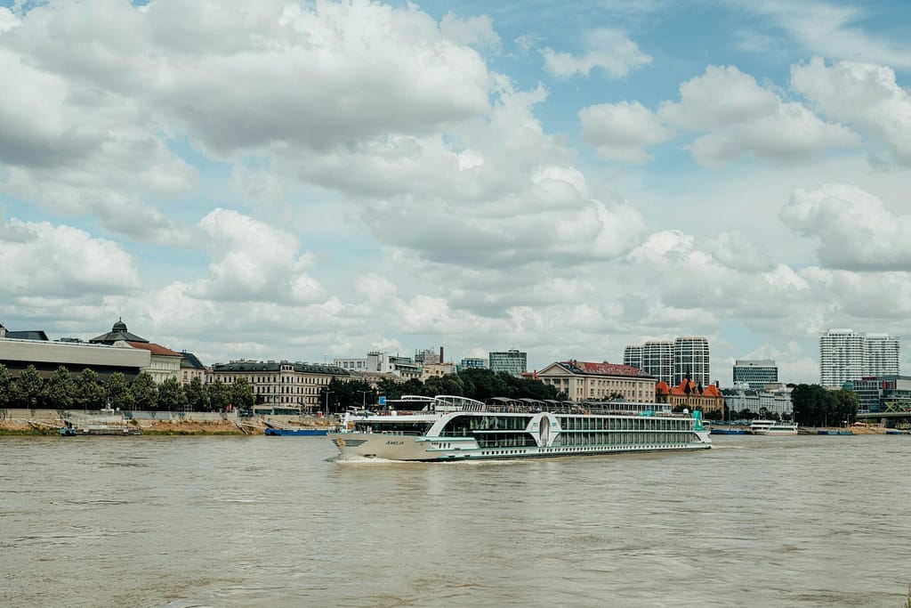 Scenic view of a cruise ship sailing the Danube River against the Bratislava skyline under a cloudy sky.