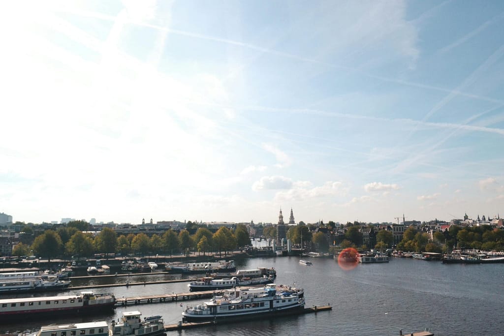 Scenic view of boats on a canal in Amsterdam with trees and historic buildings in the background.