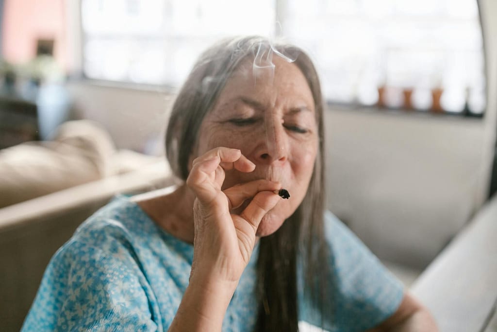 Elderly woman enjoying a marijuana joint, embracing relaxation indoors.