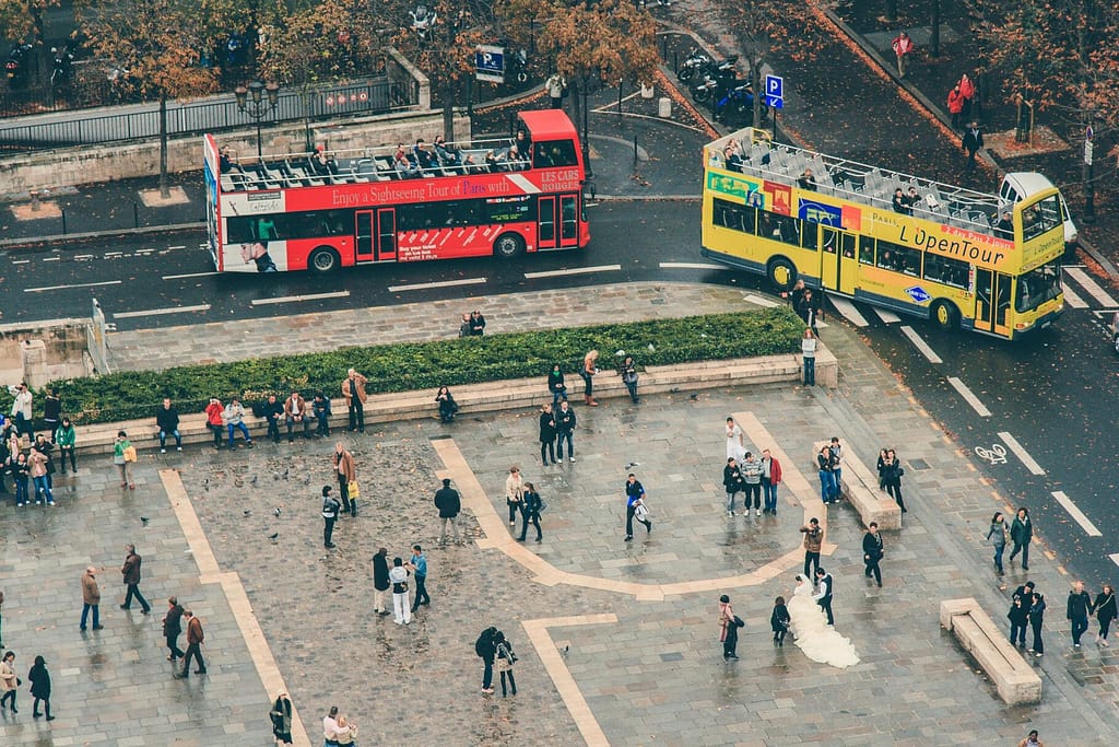 Aerial view of a bustling city square with tour buses and pedestrians in autumn.