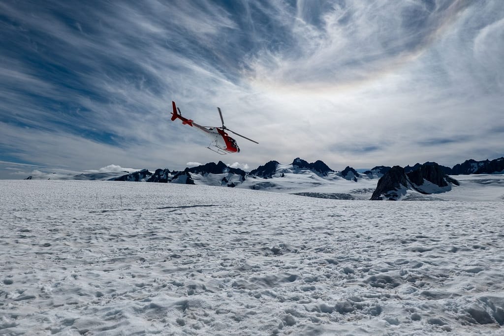 Helicopter flying over snowy Fox Glacier with stunning mountain backdrop in New Zealand.