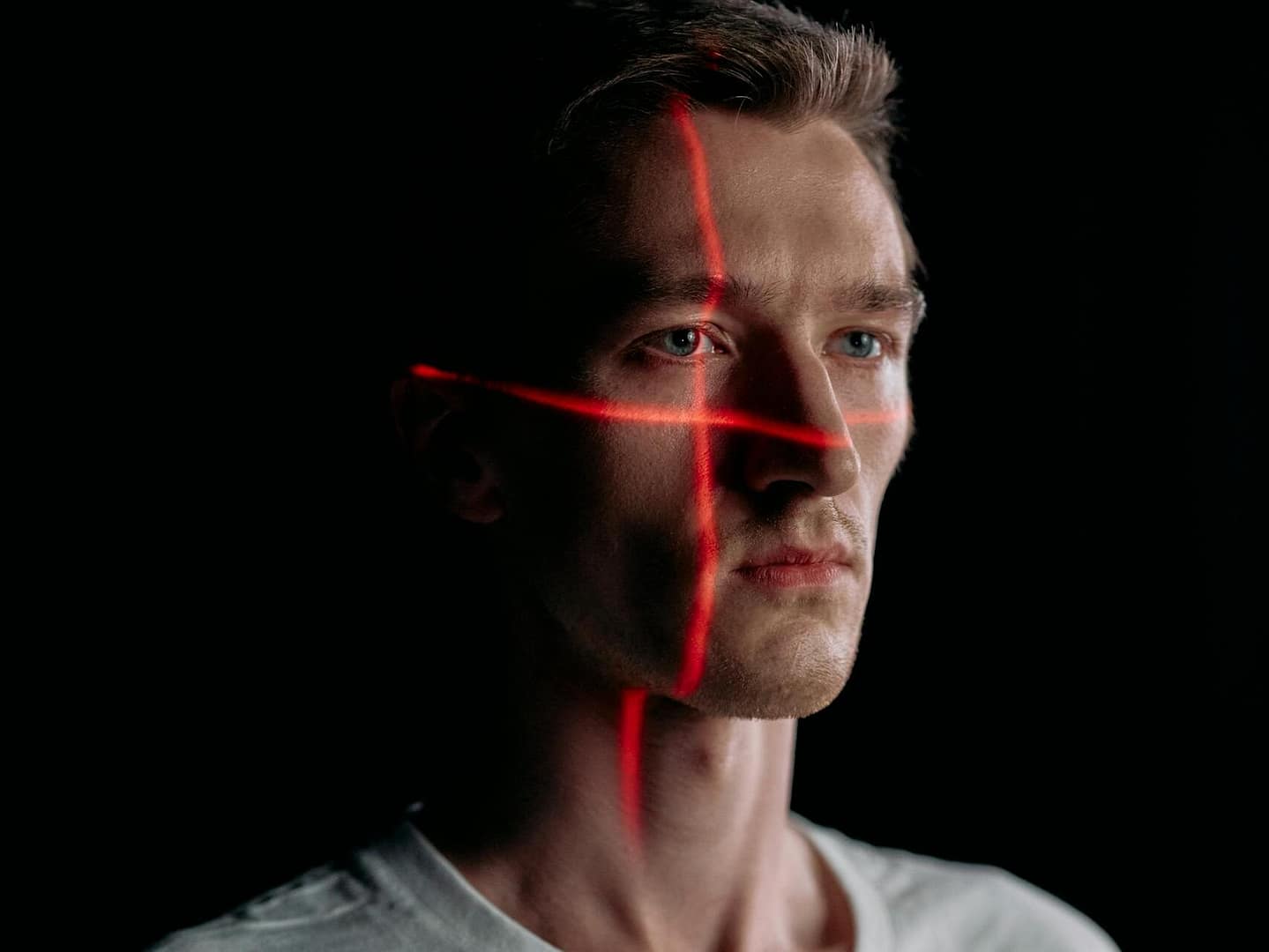 Studio portrait of expressionless man with red laser lines on face in low light.