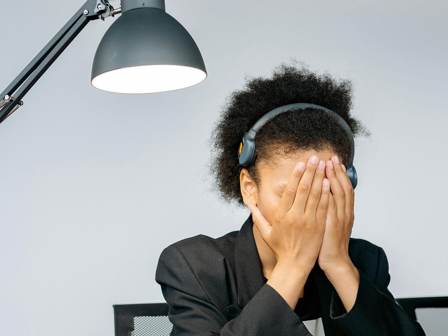 A tired call center employee covering her face with hands in frustration, wearing a headset in an office.