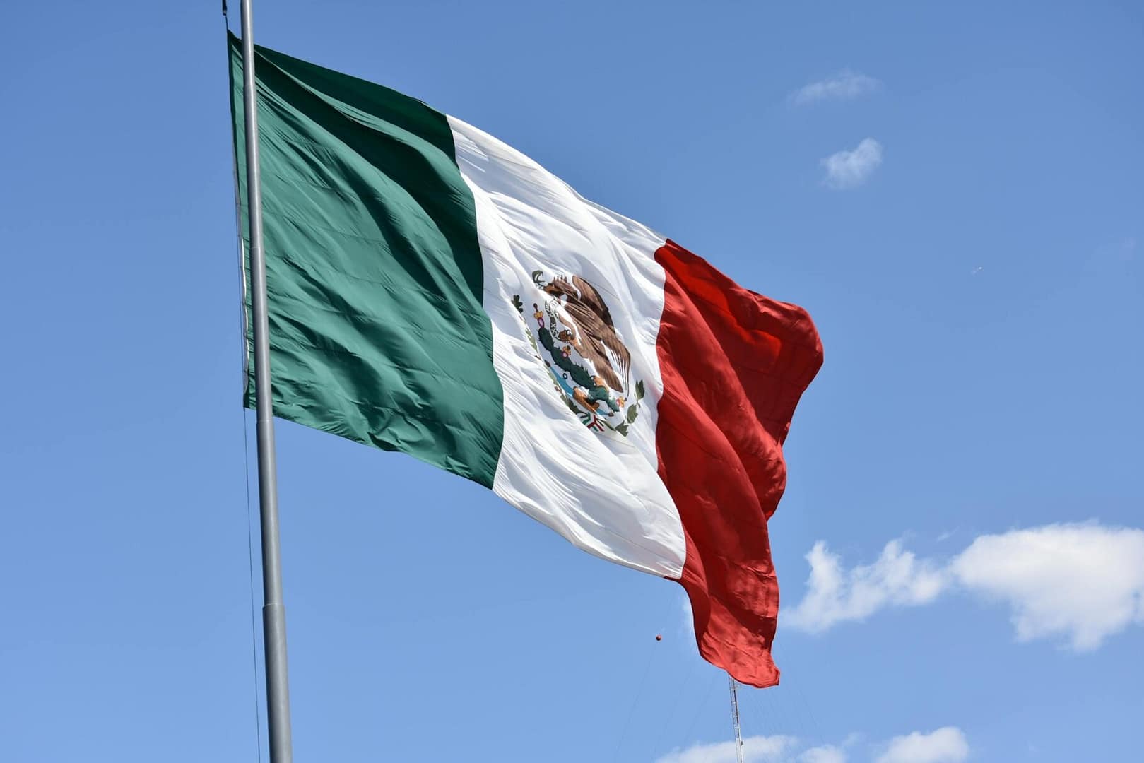 Vibrant Mexican flag waving proudly against a clear blue sky in Ciudad de México.