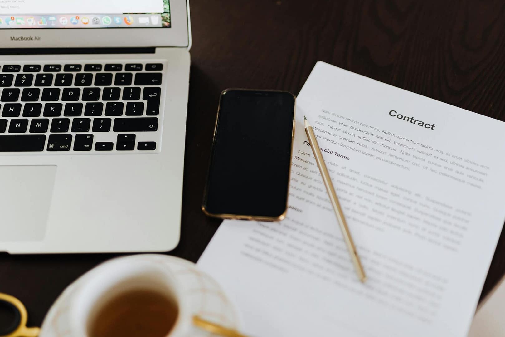 Close-up of a workspace with a contract, laptop, smartphone, and cup of tea.