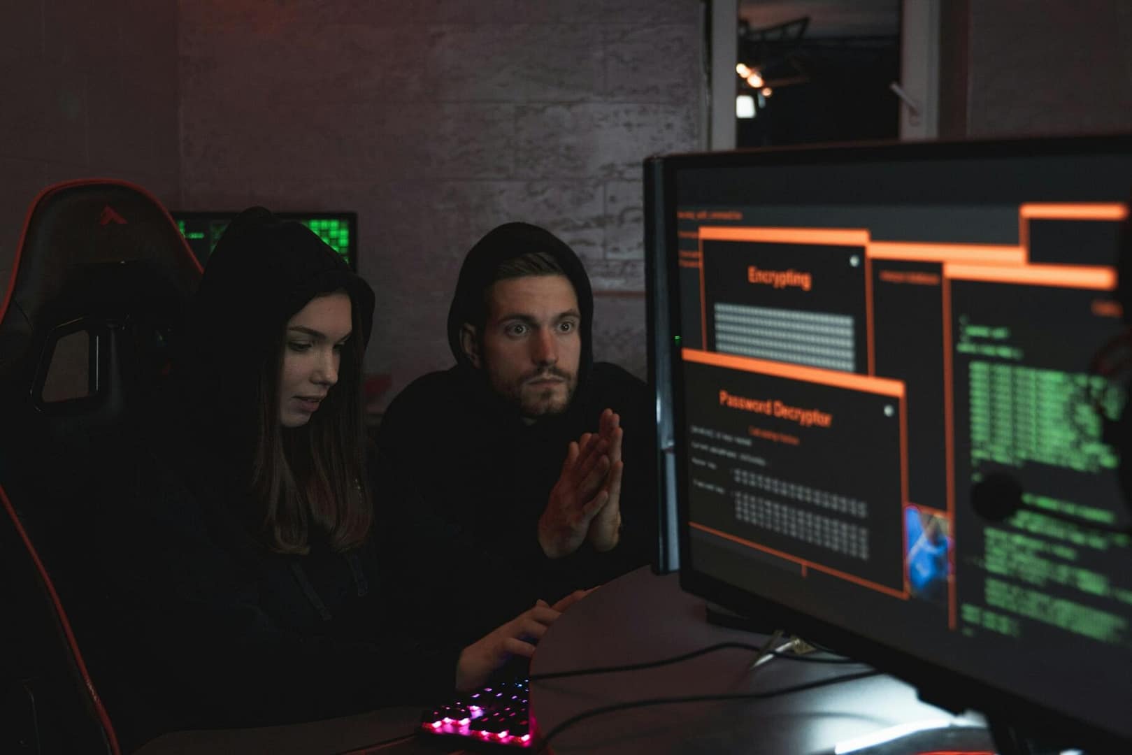 Cybersecurity experts in hoodies analyzing encrypted data on computer screens in an indoor setting.