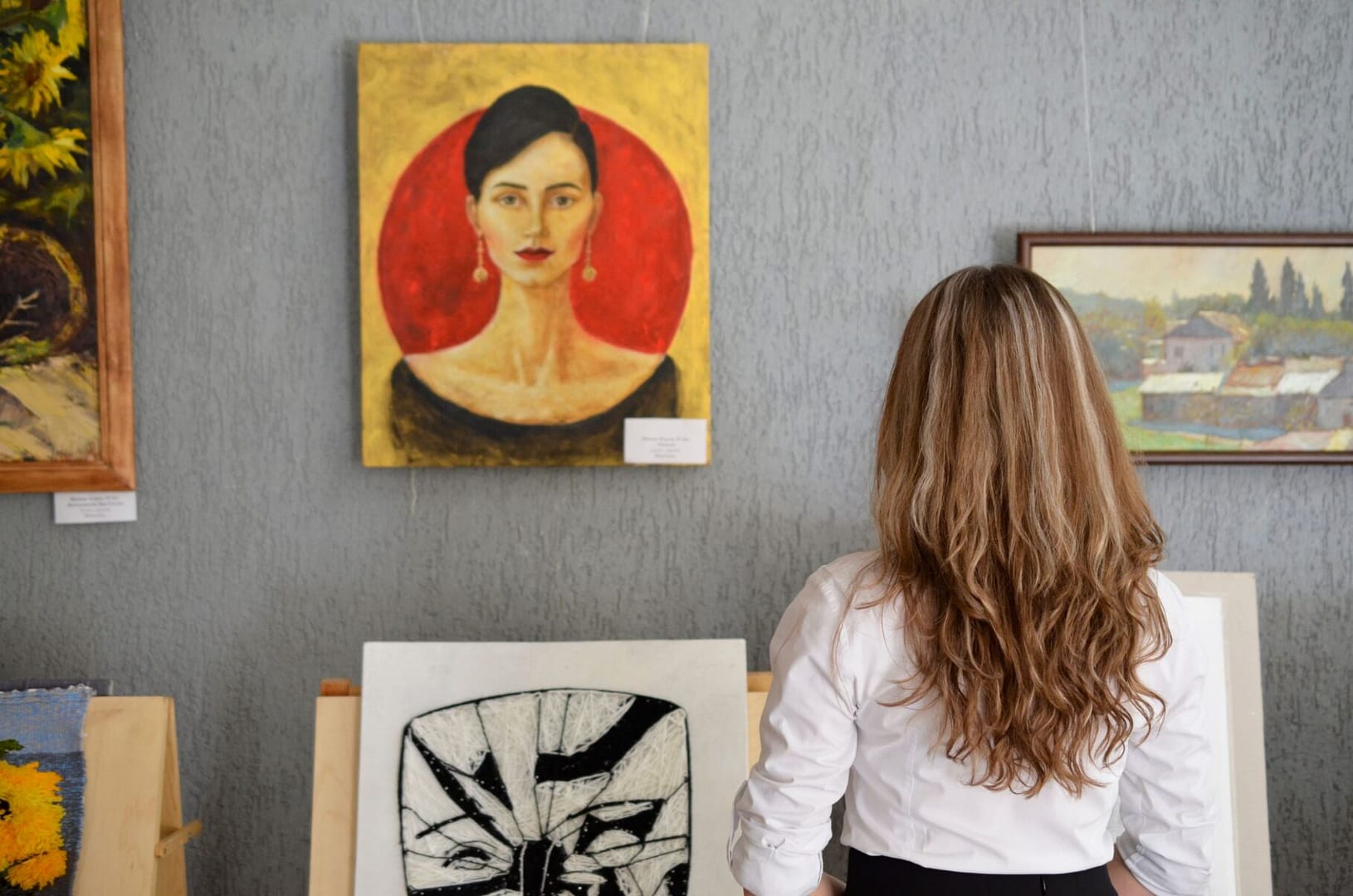 A woman views paintings in an art gallery, appreciating various art styles on display.