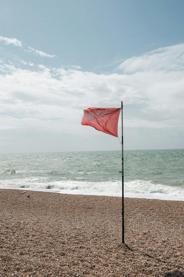 A striking red flag flutters on a pebble beach, signaling rough seas ahead.
