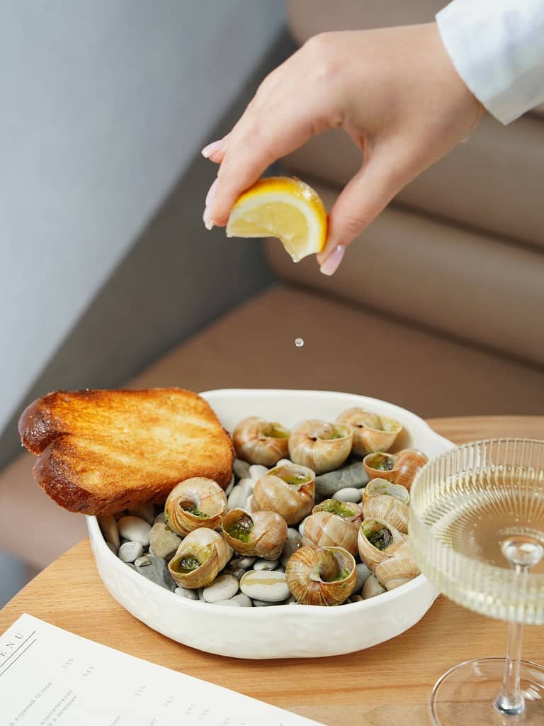 woman squeezing lemon juice in a bowl of escargot