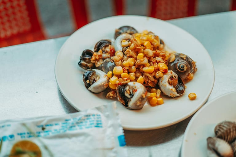 a plate of escargots with corn kernels and fried garlic