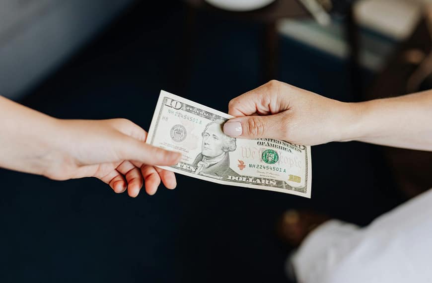 Two people exchanging a ten dollar bill in a close-up hand-to-hand transaction.