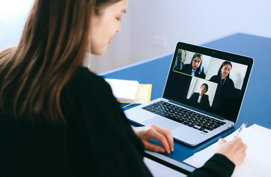 A woman engaging in a video conference using a laptop at home, taking notes.
