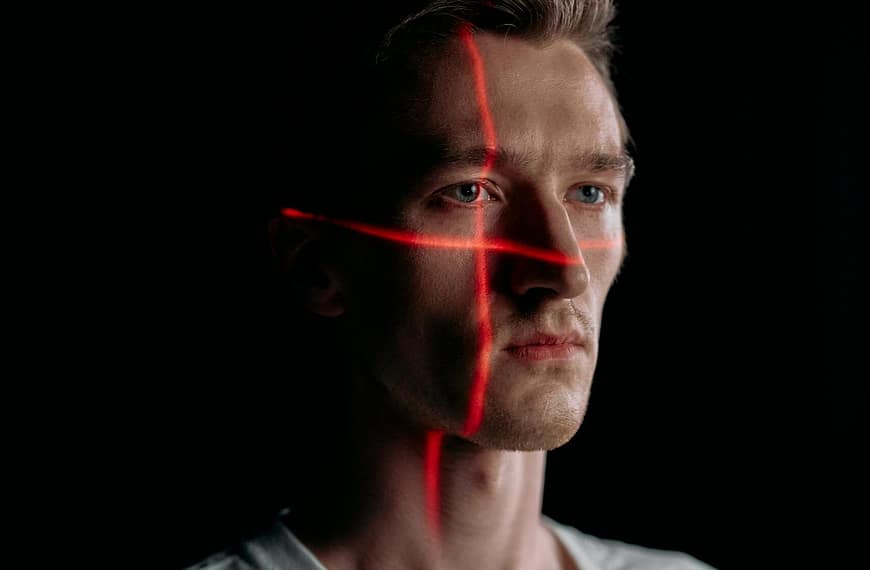 Studio portrait of expressionless man with red laser lines on face in low light.