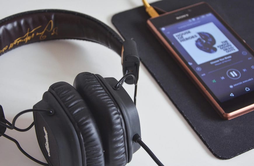 A close-up of headphones and a smartphone playing music on a desk.