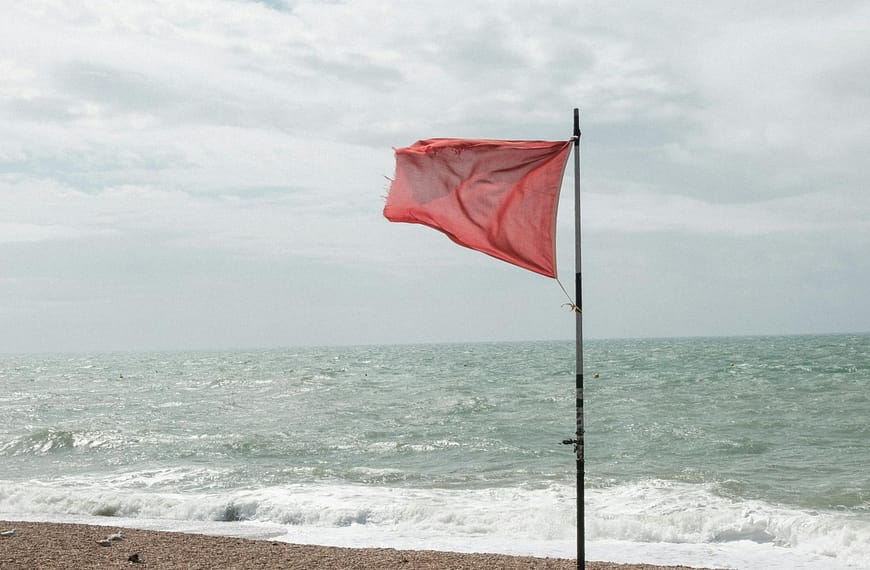 A striking red flag flutters on a pebble beach, signaling rough seas ahead.