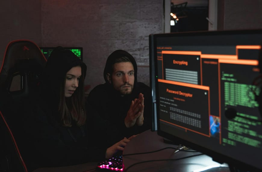 Cybersecurity experts in hoodies analyzing encrypted data on computer screens in an indoor setting.