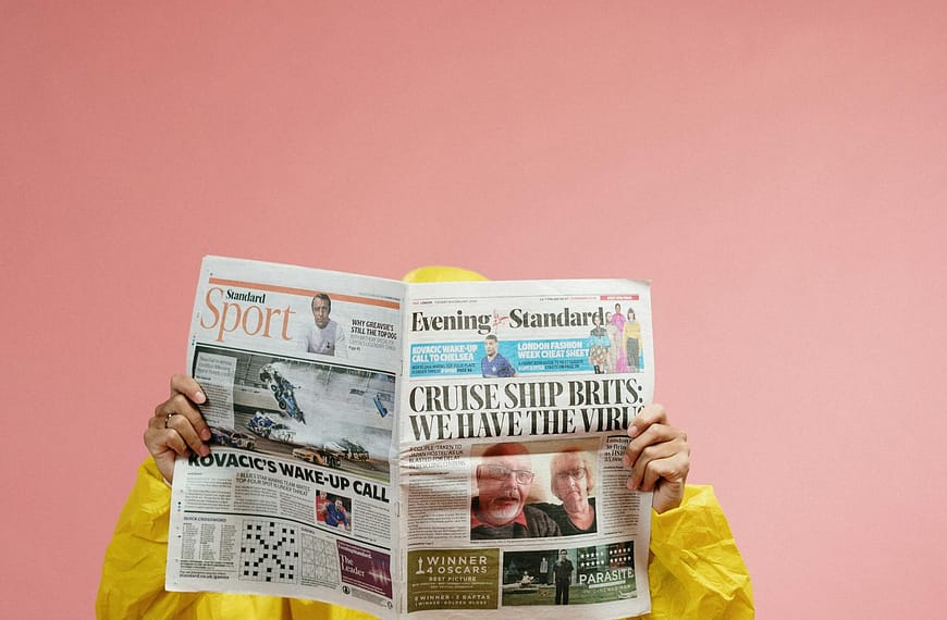 Individual in protective suit reads newspaper with pandemic headline against pink backdrop, symbolizing COVID-19 era.