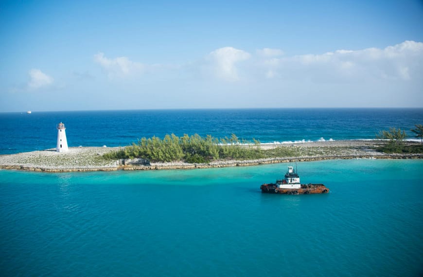 Scenic view of a tranquil island landscape featuring a lighthouse and a lone tugboat on a clear day.