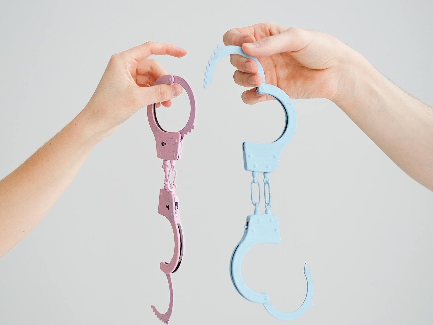 Two hands hold playful pastel-colored handcuffs against a neutral background.
